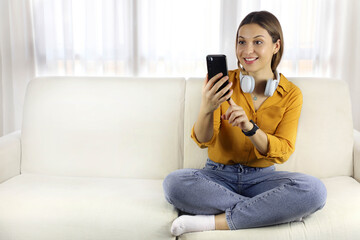 Canvas Print - Brazilian young woman using telephone sitting on sofa at home. Copy space.