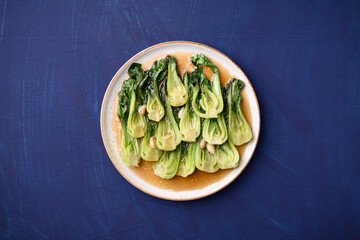 Wall Mural - Stir fried bok choy with soy sauce on plate with blue background, Asian vegan food, Top view