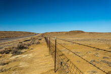 Vintage Barbwire Fence Cutting Through Open High Desert Landscape With Brush In Rural New Mexico On Clear Blue Day