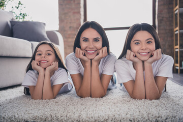 Wall Mural - Photo of charming cheerful lady cute little girls lying on floors arms on cheeks toothy smile look camera have fun indoors