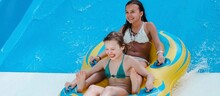 Two Little Girls On Tube On Water Slide At Aquapark. Summertime, Vacation, Entertainment, Childhood Concept. Colorful Banner.	