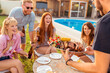 © Impact Photography - Host bringing plate of grilled meat to guests at backyard barbecue party