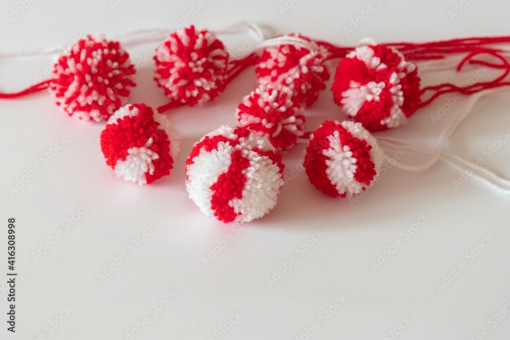 Close up red and white pompoms as martenitsa - bulgarian folklore tradition in March Baba Marta day. Shallow depth of focus, colorful yarn strains in couple of balls, light background.