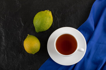 A white cup of hot tea with two green lemons