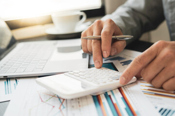 Asian male finance staff is calculating by using a calculator. Investment results to report to his boss at the meeting. On the table in the office, the concept of calculating investment results