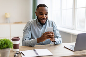 Poster - Happy African Businessman Using Phone App Sitting At Workplace Indoors