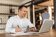 © bnenin - Smiling man working with laptop and taking notes, portrait.