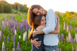 Young mother embracing her child outdoor. Woman and teenage girl on summer field with blooming wild flowers green background. Happy family mom and daughter playing on meadow.