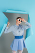 © LIGHTFIELD STUDIOS - young woman in trendy clothes and sunglasses posing near blue ripped paper on grey background