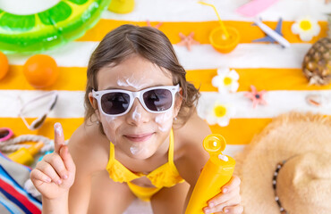 Poster - A child girl smears sunscreen on her skin. Selective focus.