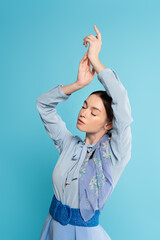 glamour woman posing with closed eyes and raised hands isolated on blue