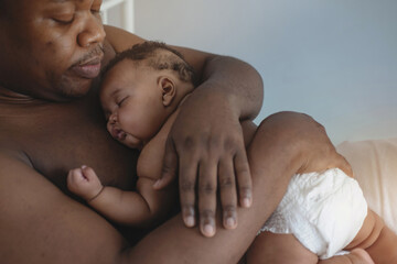 father lying on bed holds his baby daughter, 4 mouth baby on his chest, man is not wearing a shirt