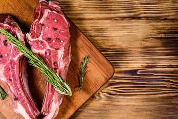 Wall Mural - Raw ribeye steak, spices and rosemary on cutting board. Top view