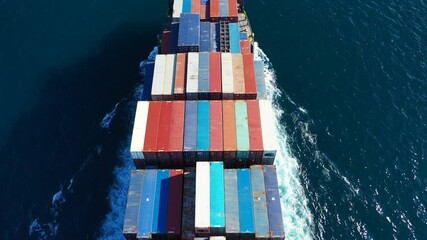 Wall Mural - Aerial top down video of Container cargo Ship carrying load in truck-size colourful containers in deep blue open ocean sea 