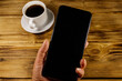 © olyasolodenko - Hand with modern smartphone and cup of coffee on a rustic wooden table