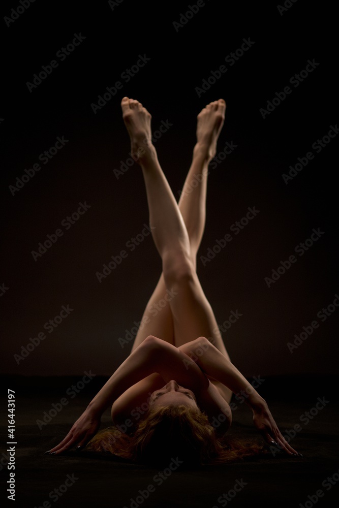Naked woman lying on floor in dark studio - obrazy, fototapety, plakaty 