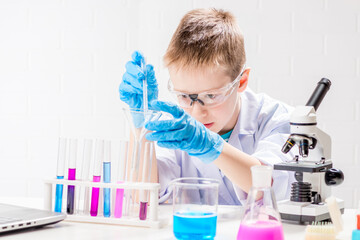 Wall Mural - a schoolboy with a microscope examines chemicals in test tubes, conducts experiments - a portrait on