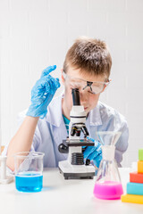 Wall Mural - a schoolboy with a microscope examines chemicals in test tubes, conducts experiments - a portrait on