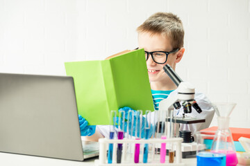Wall Mural - a schoolboy with a microscope and book examines chemicals in test tubes, conducts experiments - a po