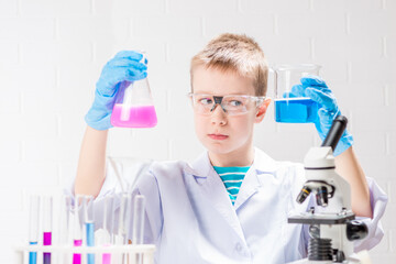 Wall Mural - a schoolboy with a microscope examines chemicals in test tubes, conducts experiments - a portrait on