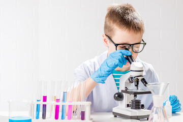 Wall Mural - a schoolboy with a microscope examines chemicals in test tubes, conducts experiments - a portrait on