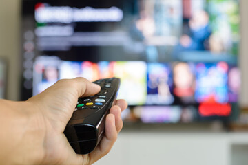 He, a man, is using a remote control to scroll through TV programs during the quarantine period to reduce the spread of the virus.