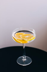 Cocktail with clear drink and two orange slices is poured into trendy champagne glass on black table.