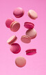 Colorful sweet macarons or macaroons, flavored cookies floating in the air on pink background.