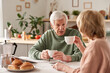 © AnnaStills - Happy senior couple sitting at the table drinking tea and talking to each other in the kitchen at home