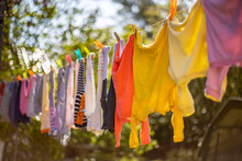 Baby Cute Clothes Hanging On The Clothesline Outdoor. Child Laundry Hanging On Line In Garden On Green Background. Baby Accessories.