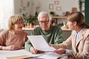 Senior couple sitting at the table and discussing documents with real estate agent they making a will