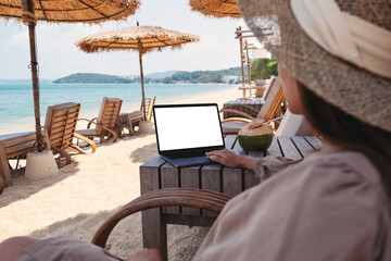 Mockup image of a woman using and touching on laptop touchpad with blank desktop screen while sitting on the beach