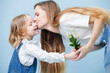 © zzzdim - Little girl gives her mother bouquet of wild camomiles, she kisses her for it. Both look happy. Over blue background.