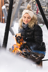 Beautiful woman warming up by the fire pit during cold winter day