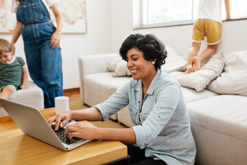 Wall Mural - Woman working on laptop with her family in background