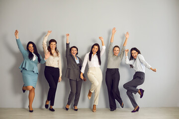 Wall Mural - Success, business development, woman office workers staff. Smiling positive women workers jumping and celebrating business win in corporate project with hands raised over grey wall background