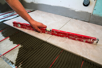 Canvas Print - Ceramic tiles and tools for tiler. Worker hand installing floor tiles. Home improvement, renovation - ceramic tile floor adhesive, mortar, level.