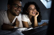 © Zoran Zeremski - Couple lying on bed in bedroom looking at laptop at night.