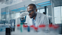 Modern Medical Research Laboratory: Portrait Of Male Scientist Looking Under Microscope, Analysing Samples. Advanced Scientific Lab For Medicine, Biotechnology, Microbiology Development