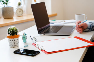 Canvas Print - a young man in a shirt in a bright office works at a laptop and makes notes in a notebook, the menta