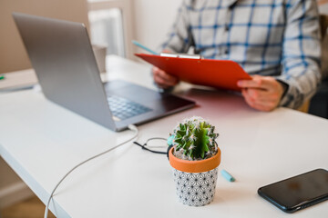 Canvas Print - a young man in a shirt in a bright office works at a laptop and makes notes in a notebook, the menta