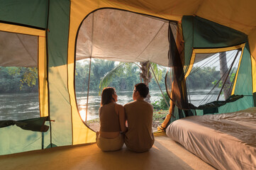Wall Mural - Young asian couple relaxing inside a tent on campsite in natural park