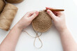 Women's hands knit a circle crochet with a wooden jute hook.