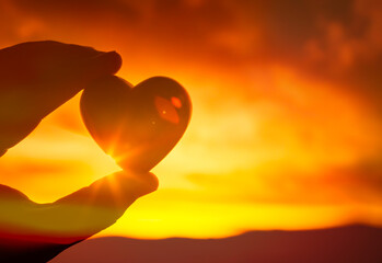 Hand holding heart up to beautiful sunset sky 