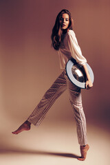 Woman with mirror posing in striped pants at sunset