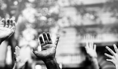 Open palm of a black hand and white hands raised in the air asking for freedom. Multicultural hands in a demonstration on street in black and white. Stop racism. Stop repression.