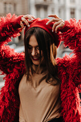 Portrait of charming woman with red lips, dressed in red eco-coat and beret. Lady in great mood walks around city