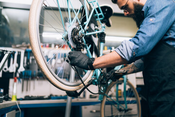 Young beard bicycle mechanic repairing bicycles in a workshop..