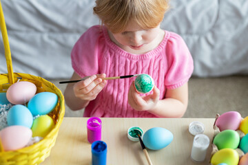 Easter holiday craft at home. Little girl in Easter bunny ears painting colored eggs.