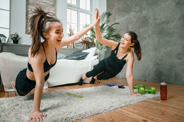 Two women friends at home chatting, smiling and makes training in bedroom. Two women girlfriends are stretching,  look at each other, give five